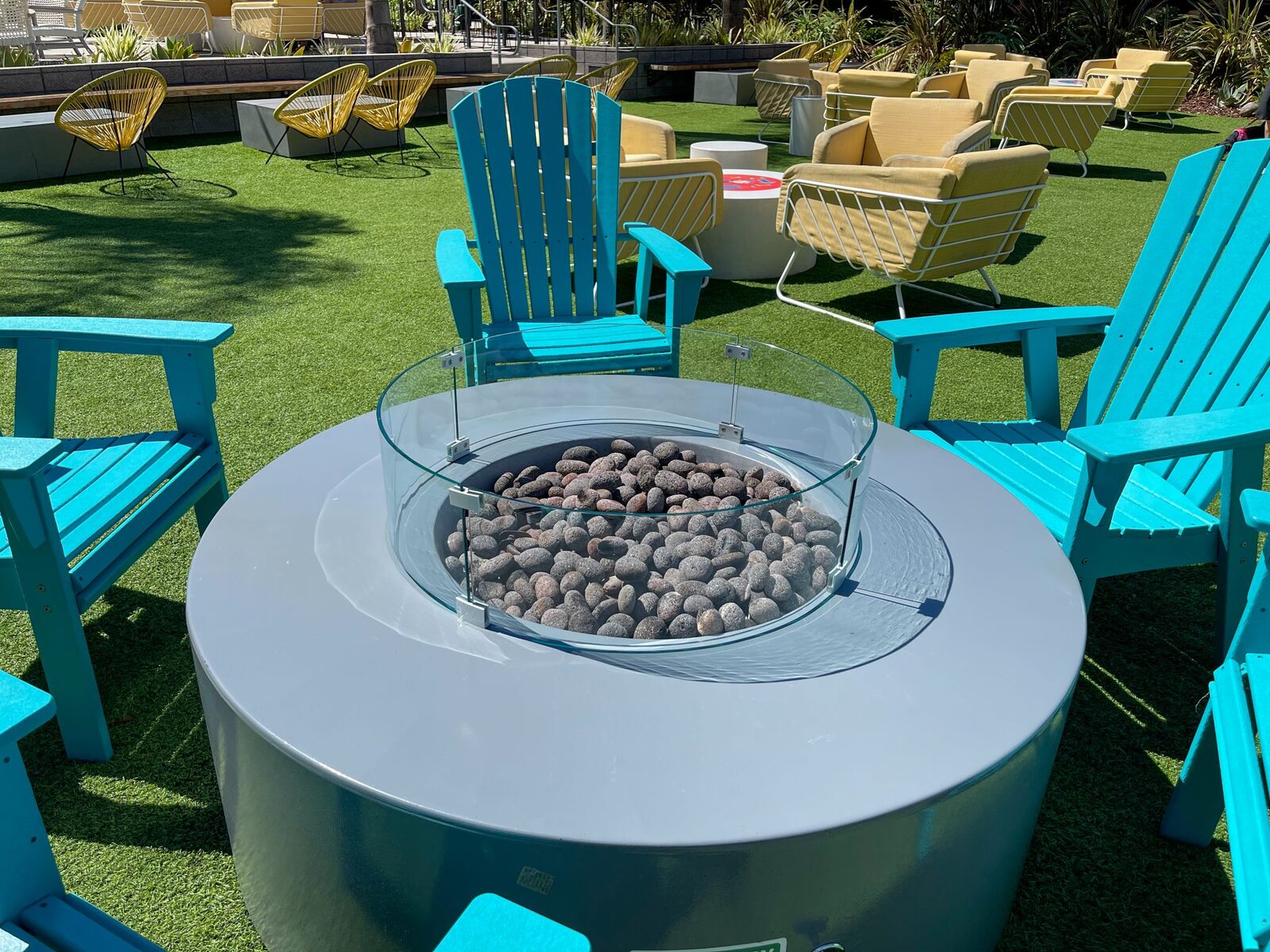Backyard fire pit patio with Adirondack chairs and a lush green lawn in the Bay Area